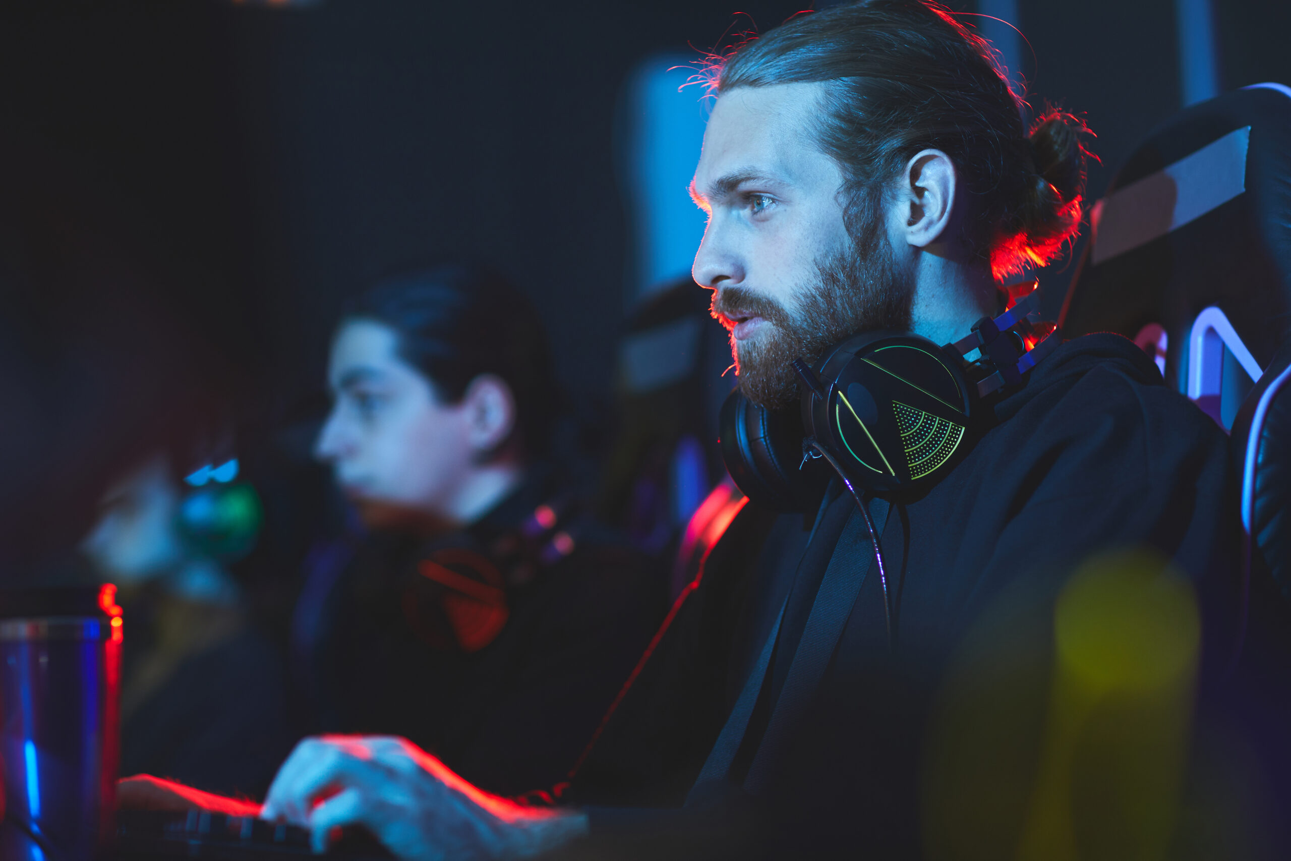 E-Sport-Spieler sitzt konzentriert am PC, trägt Headset und wird von farbigem Neonlicht beleuchtet.