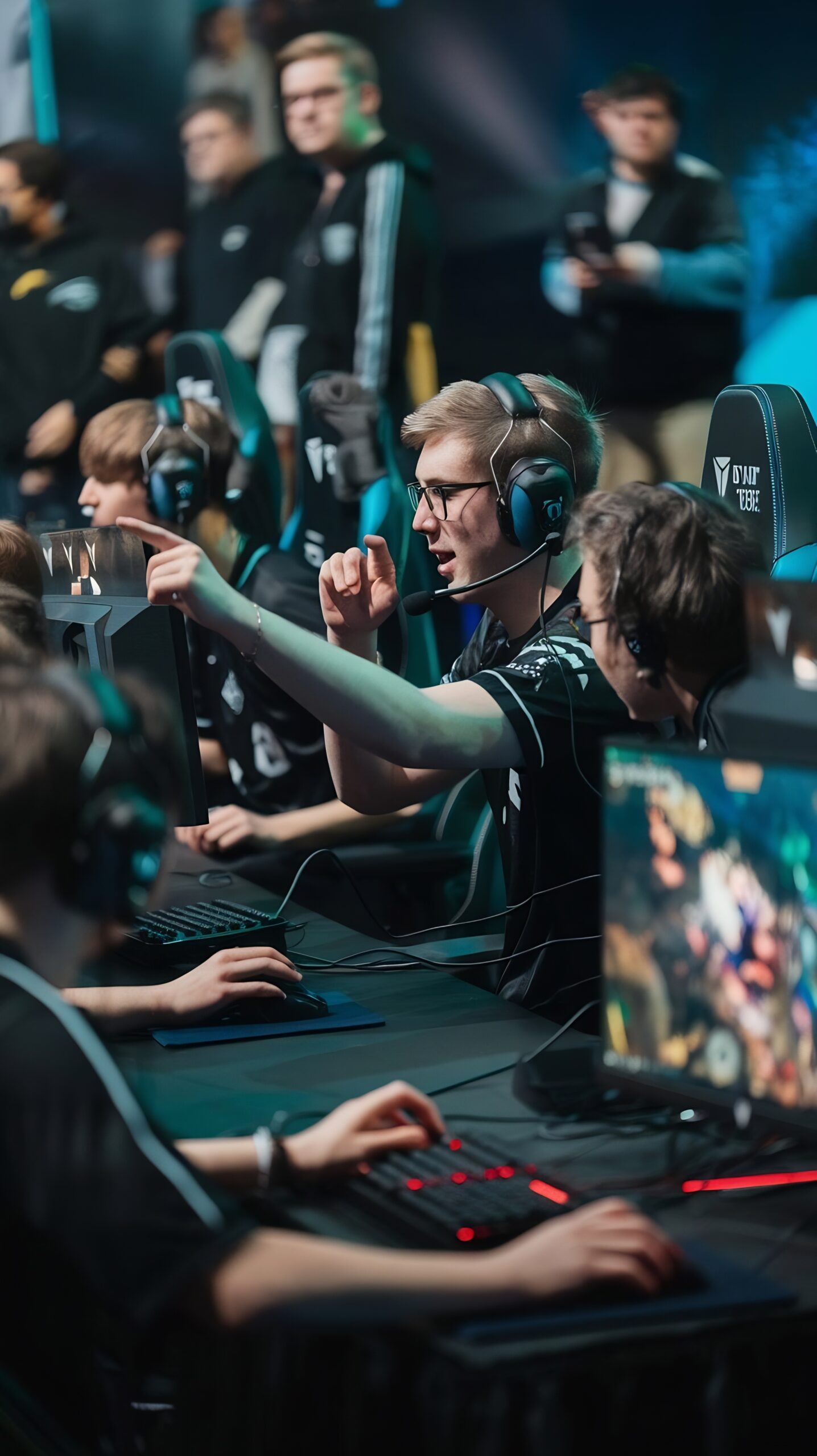 Spieler in E-Sports-Team sitzen an PCs, besprechen Spielzüge und zeigen gestikulierend auf den Bildschirm.